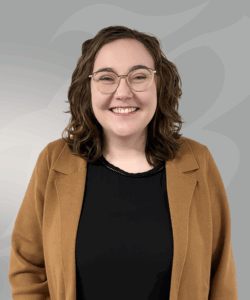 women standing in front of gray wall with black shirt and brown jacket on.